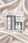 ALIGN Age Reverse System skincare set in a white box, featuring a cleanser, serum, and cream, displayed on a draped champagne satin fabric background.