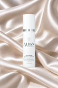 A white cylindrical skincare bottle labeled 'ALIGN skincare Collagen Quench Serum' standing upright on draped champagne satin fabric.