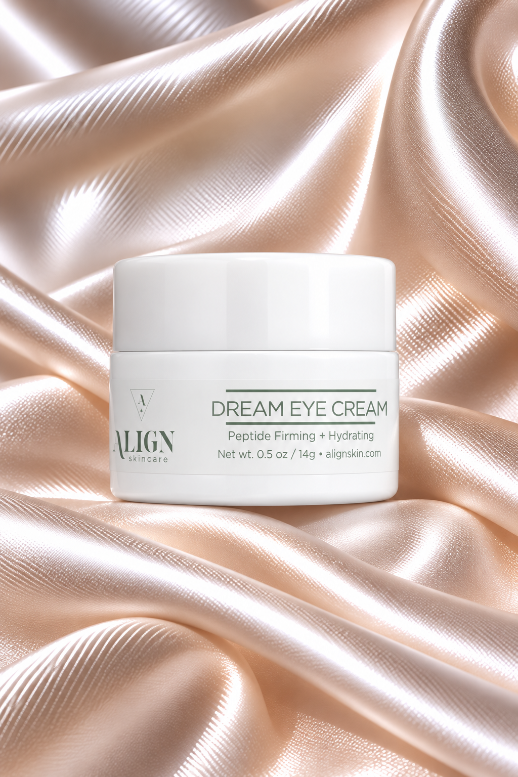A white jar of ALIGN Cosmetics Dream Eye Cream sits on draped champagne satin fabric.