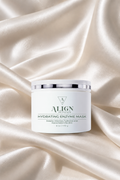 A white jar of ALIGN Skincare Hydrating Enzyme Mask with a silver lid, set against a draped cream satin fabric background.