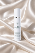 A white cylindrical skincare bottle labeled ALIGN skincare Invigorating Cleanser, standing upright on draped champagne satin fabric.