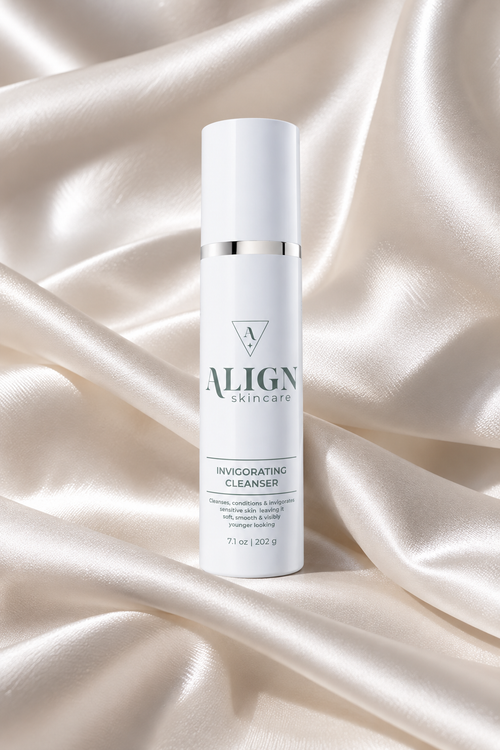 A white cylindrical skincare bottle labeled ALIGN skincare Invigorating Cleanser, standing upright on draped champagne satin fabric.