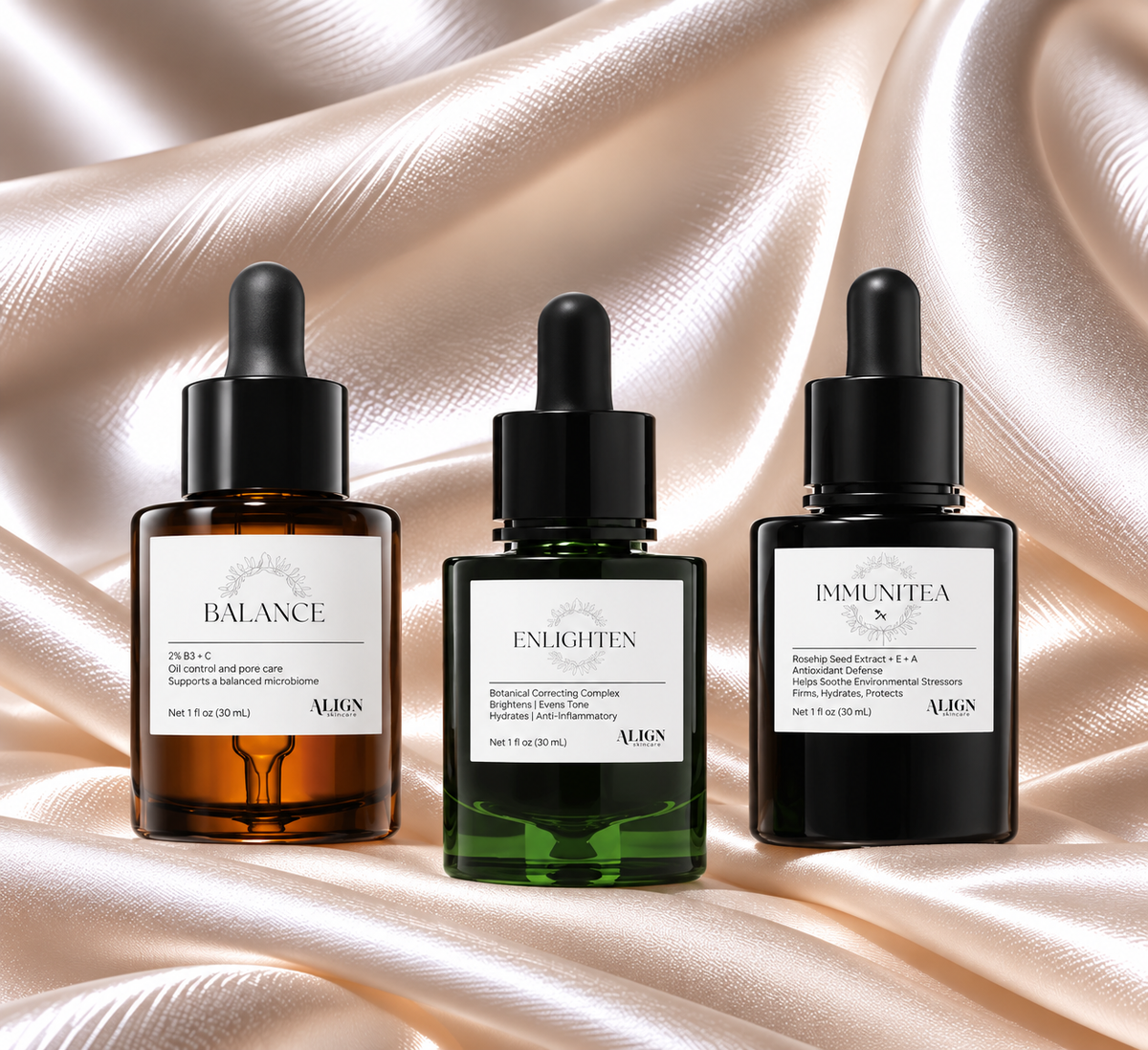 Three VION skincare dropper bottles arranged side by side on draped champagne satin fabric. The bottles are labeled Balance, Enlighten, and Immunity, with amber, green, and black glass and black droppers.