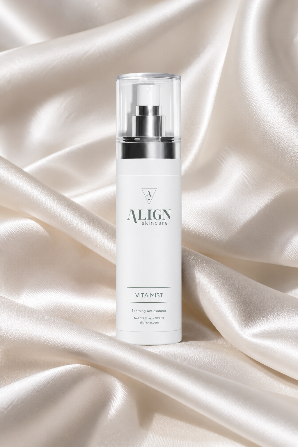 A white cylindrical skincare pump bottle labeled ALIGN SKINCARE VITA MIST, standing upright on draped champagne satin fabric.